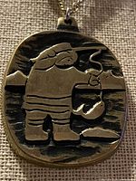 Front of brass pendant showing Inuit fisherman design