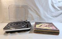Turntable with open dust cover beside stacked LPs, front view