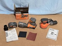 Overall lot layout showing two sanders, battery, accessories, manuals, and box