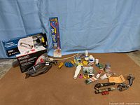 Wide view of entire lot showing boxed Ridgid drain cleaner, sprinkler, Drain Weasel kit and loose plumbing parts