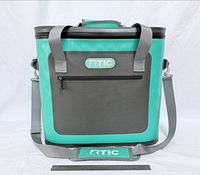 Front view of RTIC seafoam soft-sided cooler showing logo, front pocket, handles, shoulder strap and ruler for scale
