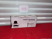 Front view of boxed toner cartridge showing moustache logo