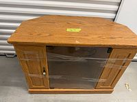 Front view of oak corner TV stand showing glass door and wood grain