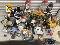 Tabletop spread showing drill, heat gun, lanterns, spray cans, adhesives, ammunition, hand tools, rope, string light and various packaged supplies