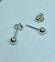 Two sterling silver ball stud earrings lying on white surface, posts and butterfly backs visible