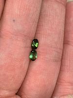 Two oval green tourmaline gemstones on fingertip