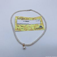 Necklace laid flat with certificate showing pearls and clasp
