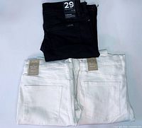 Overview of three jean pairs: one black, two white, showing back pockets and size tags