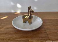 Front angled view of white ceramic dish with gold llama figurine