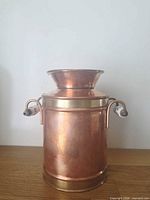 Front view of copper milk can highlighting brass band and ceramic handles