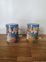 Front view of both cylindrical shakers showing cat and dog graphic, blue lids and handles