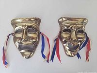 Front view of both brass masks showing expressions and ribbons