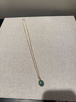 Full view of gold necklace with green pendant laid flat