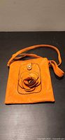 Full view of orange leather purse with strap and flower applique