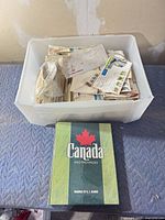 Plastic bin with loose stamps and green Canada album