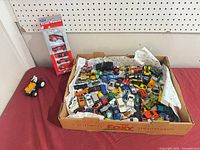 Open box filled with numerous small die-cast vehicles plus sealed Team Power blister pack and loose tractor visible