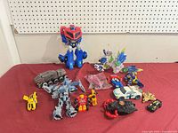 Group shot of all Transformers figures and accessories on red surface
