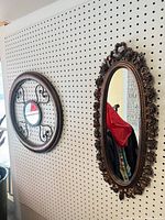 Both mirrors hanging on pegboard, round on left, oval on right