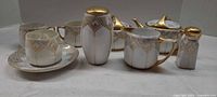 Front angled view of full porcelain set showing cups, saucer, pots, shakers, and creamer