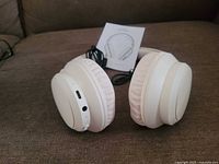 Off-white wireless headphones showing earcups, ports and manual
