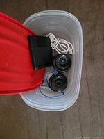 Top view of plastic tub showing both cameras, charger, white cable and blue cable