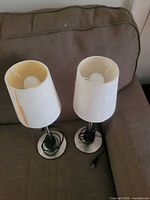 Two table lamps with white shades (tears visible) on couch