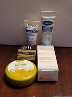 Five primary items outside bag: Uriage tube, Cetaphil tube, e.l.f. box, Kamill tin, Clarins box