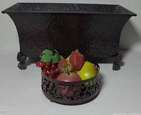 Rectangular metal planter behind round pierced bowl with faux fruit