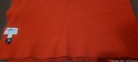 Full view of folded orange-red wool blanket showing color and texture