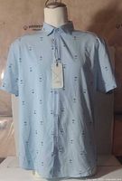 Front view of light blue palm tree print shirt on mannequin with tag
