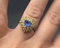 Ring worn on finger showing blue center stone and crystal halo