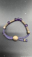 Full bracelet laid flat showing cord, amethyst beads, silver spacers and slider bead