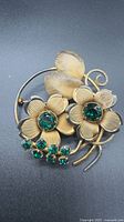 Front view of gold-tone floral brooch displaying green rhinestones and design details