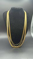 Full view of necklace on display bust showing three flat gold tone strands