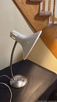 Full view of desk lamp showing white flared shade, chrome gooseneck, chrome base