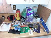 Wide view of countertop with assorted items including Swiffer box, lantern, earmuffs, dust mask, bulbs, hardware