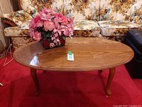 oak oval coffee table with floral arrangement centered on top, showing sofa backdrop