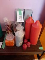 Front view showing two red pillars, blue and white pillars, red votives, orange jar candle, burgundy bag, and boxed candles