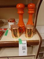 Front view of orange pepper mill and salt shaker, copper/brass shakers with handles, and ceramic/copper shaker
