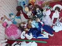 Group shot of porcelain dolls laid out on red carpet showing variety of dresses and sizes