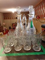 Front view showing three cut-glass decanters with stoppers and eight pressed-glass tumblers
