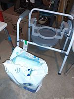 Front view of folding steel commode and partial pack of TENA pads