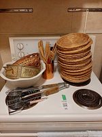 All items grouped on stovetop showing wicker plates, utensils, bowls, baskets and metal tools