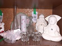 Shelf showing two white Buddha statues, glass elephant holders, decanter, vases, shell ornament
