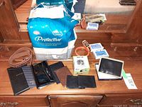 Overview of all items on dresser including package of pads, belt, wallets, watch box, cards and orange wrist light