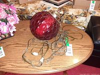Full view of red glass globe swag lamp resting on table with chain and cord visible