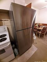 Front left view of stainless steel Midea top-freezer refrigerator beside stove