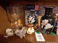 Shelf showing all items: plush seals, glass goblet, teapot, boxed vase, black vase