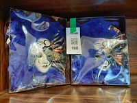 Two boxed blue feathered Venetian masks side by side