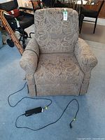 Front view of beige brown paisley power lift recliner chair with remote on floor